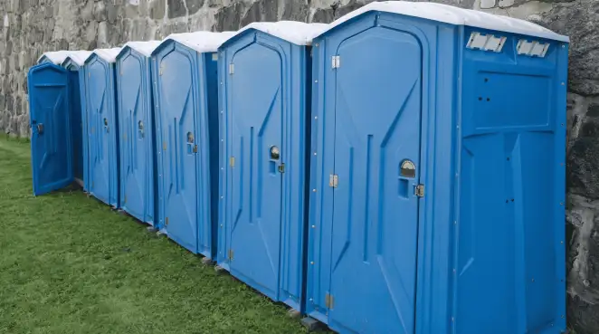 Row of blue portable toilets lined up on grass against a stone wall for event sanitation in Naperville, IL