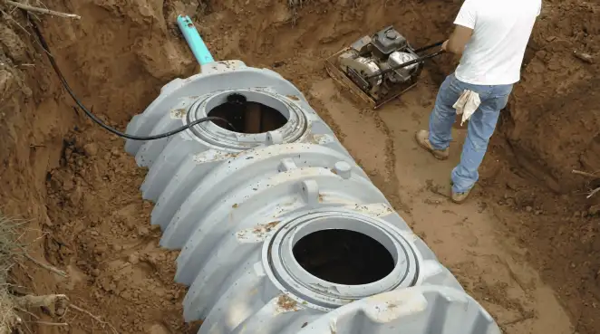 Septic tank installation showing a technician compacting soil around a new poly septic tank in an excavation pit in Naperville, IL
